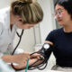 Estudante de Medicina da Unoeste mede a pressão arterial de uma paciente durante atendimento clínico, utilizando estetoscópio e esfigmomanômetro em ambiente acadêmico.
