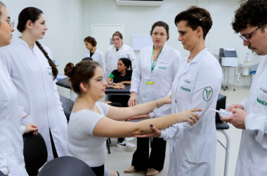 Estudantes de Fisioterapia da Unoeste em aula prática, avaliando movimentos do braço de uma colega sob supervisão de professor, em ambiente de laboratório.