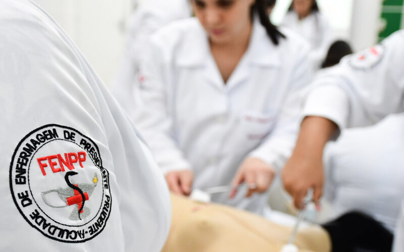 Estudantes da Faculdade de Enfermagem da Unoeste em aula prática com jaleco branco e símbolo institucional bordado no uniforme, representando o cuidado, a formação técnica e o compromisso com a Enfermagem.