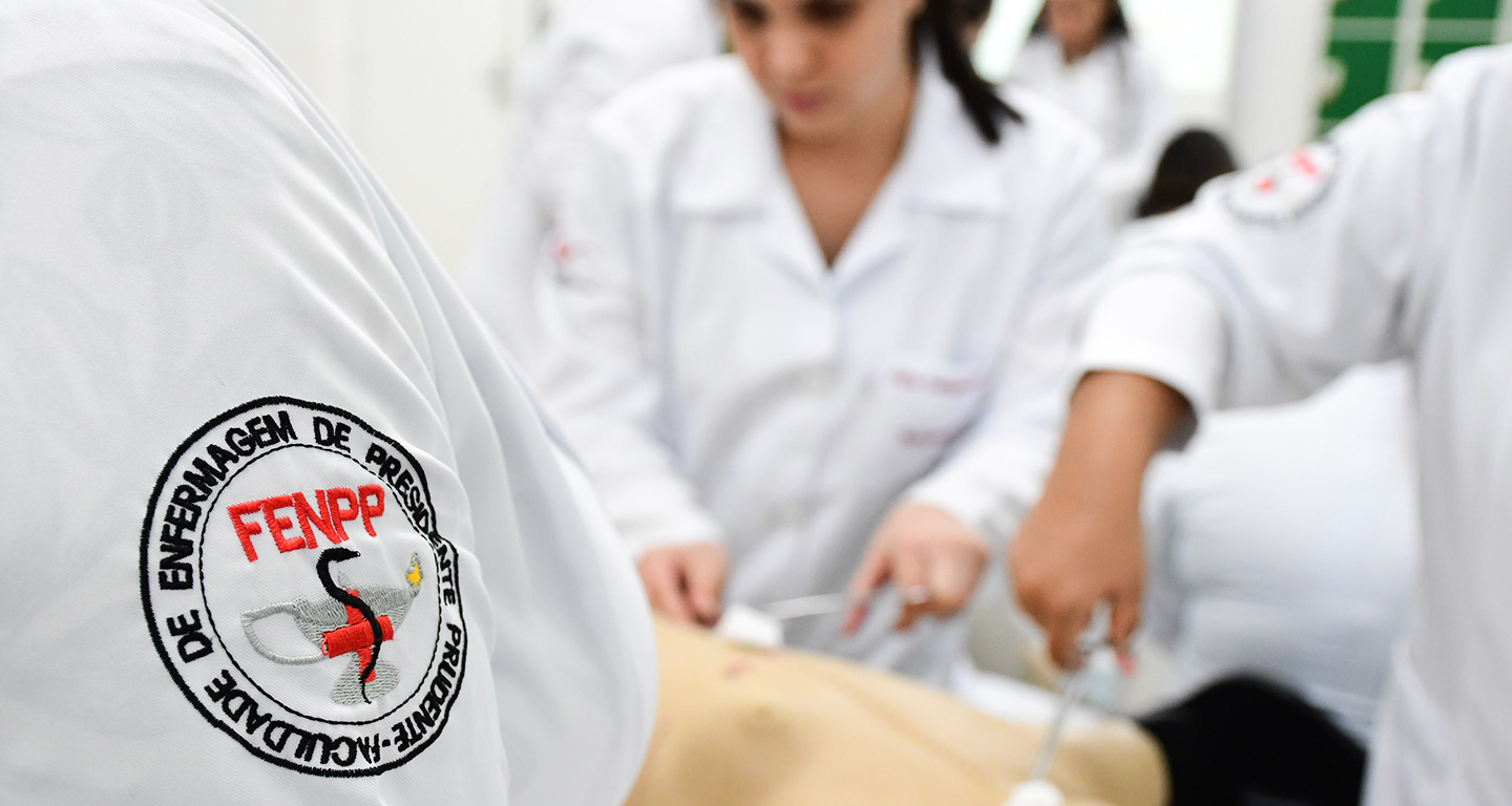 Estudantes da Faculdade de Enfermagem da Unoeste em aula prática com jaleco branco e símbolo institucional bordado no uniforme, representando o cuidado, a formação técnica e o compromisso com a Enfermagem.