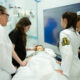 Estudantes de Medicina da Unoeste realizando prática em laboratório de simulação realística, acompanhando sinais vitais em monitor e treinando atendimento a paciente em manequim hospitalar.