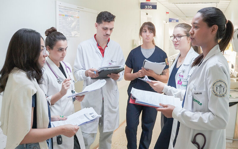 Grupo de estudantes de Medicina da Unoeste realizando discussão de caso clínico em corredor hospitalar durante atividade supervisionada do internato, evidenciando prática profissional, trabalho em equipe e aprendizado em ambiente real de saúde.