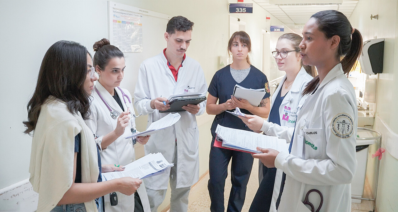 Grupo de estudantes de Medicina da Unoeste realizando discussão de caso clínico em corredor hospitalar durante atividade supervisionada do internato, evidenciando prática profissional, trabalho em equipe e aprendizado em ambiente real de saúde.