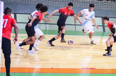 Jogo de futsal em quadra com jogadores disputando a bola em ritmo intenso, representando o foco, a velocidade e a superação presentes nos filmes esportivos.