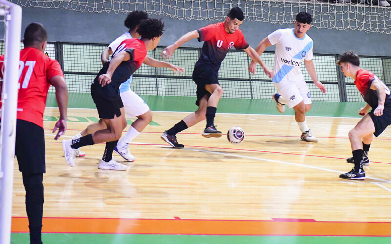 Jogo de futsal em quadra com jogadores disputando a bola em ritmo intenso, representando o foco, a velocidade e a superação presentes nos filmes esportivos.