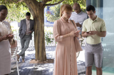 Pessoas usando smartphones em ambiente urbano, cena do episódio Nosedive da terceira temporada de Black Mirror, que aborda redes sociais, avaliações digitais e comportamento social mediado por tecnologia.