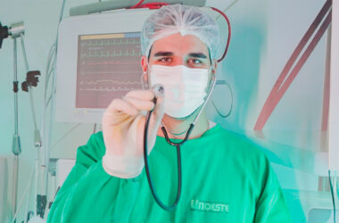 Estudante de Medicina com jaleco cirúrgico e estetoscópio em ambiente hospitalar, simbolizando a prática médica e o cuidado com a saúde.