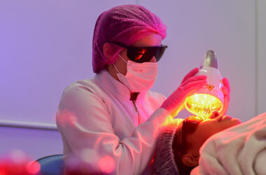 Aluna da faculdade de Estética e Cosmética realiza procedimento facial não invasivo em aula prática, utilizando equipamento estético e seguindo normas de biossegurança.