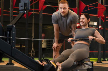 Profissional de Educação Física orientando aluna durante exercício em equipamento de treino funcional dentro de academia, com foco em saúde e desempenho físico.