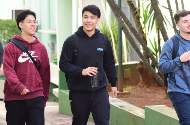 Três jovens utilizando mochilas e sorrindo caminham pelo campus da Unoeste.