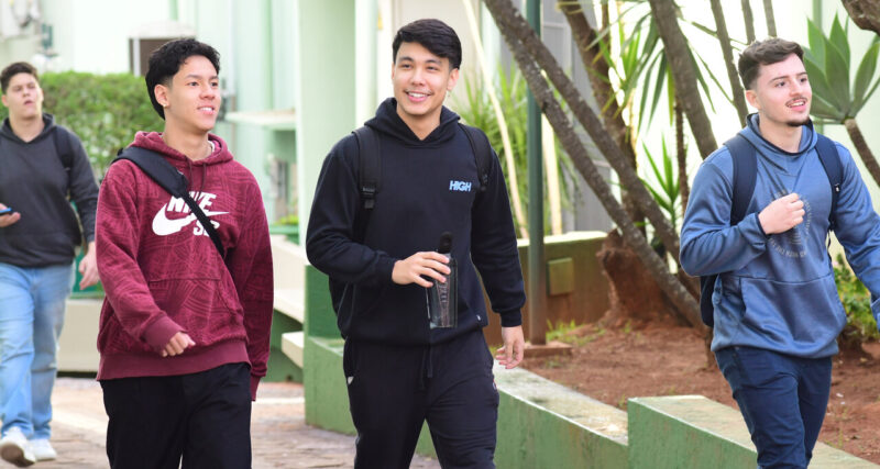 Três jovens utilizando mochilas e sorrindo caminham pelo campus da Unoeste.