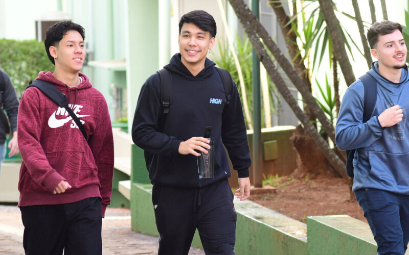 Três jovens utilizando mochilas e sorrindo caminham pelo campus da Unoeste.