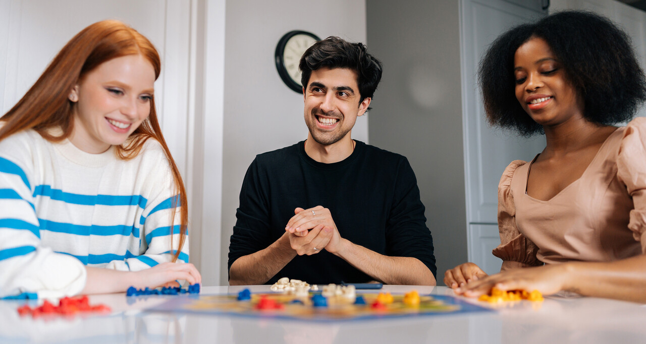 Grupo de jovens adultos interagindo em uma atividade com jogo de tabuleiro, estimulando habilidades cognitivas como atenção, raciocínio e socialização em ambiente colaborativo.