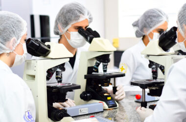 Estudantes da área da saúde utilizando microscópios em laboratório acadêmico, durante aula prática de graduação relacionada às ciências da saúde.
