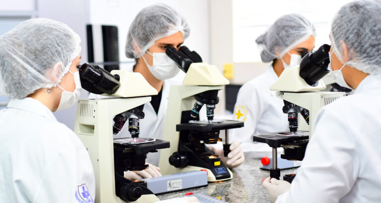 Estudantes da área da saúde utilizando microscópios em laboratório acadêmico, durante aula prática de graduação relacionada às ciências da saúde.