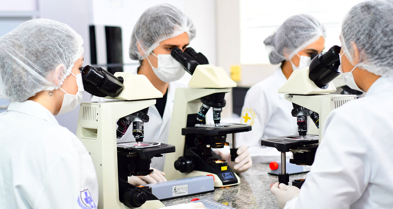 Estudantes da área da saúde utilizando microscópios em laboratório acadêmico, durante aula prática de graduação relacionada às ciências da saúde.