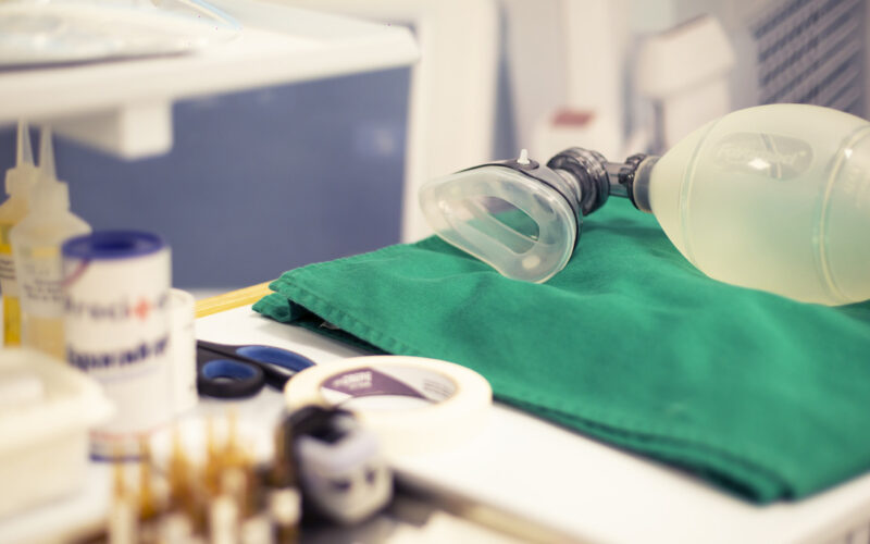 Equipamentos de anestesia organizados em bancada hospitalar, com máscara e ambu sobre campo cirúrgico verde, utilizados em procedimentos anestésicos e cirúrgicos.