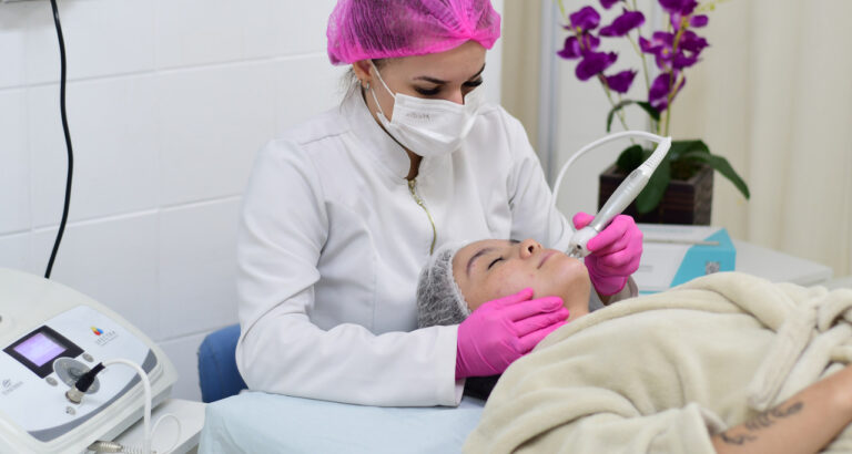 Aluna do curso de Estética e Cosmética realiza procedimento facial com equipamento estético em clínica-escola, durante aula prática supervisionada.