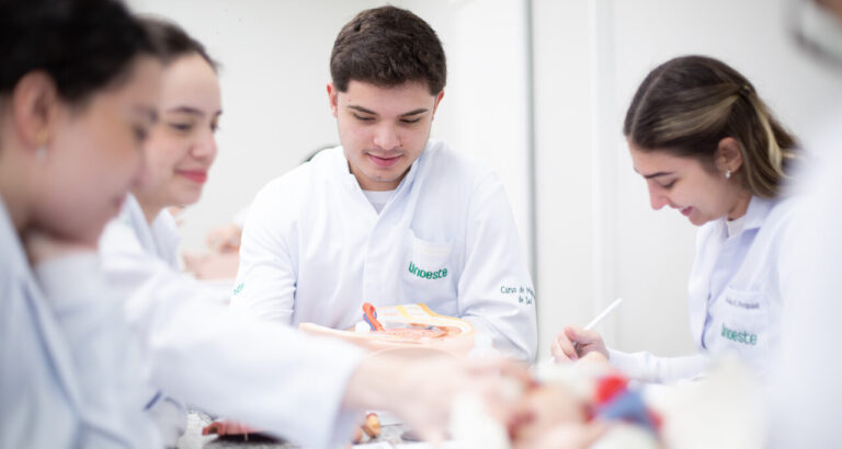 Estudantes de Medicina em aula prática, analisando modelo anatômico durante atividade em laboratório, com orientação acadêmica e foco na formação médica.