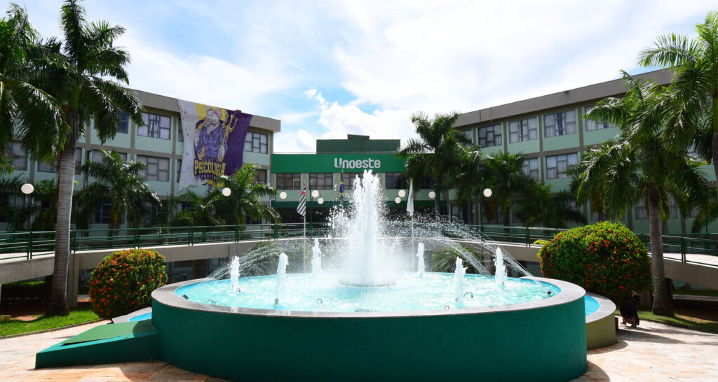 Campus 2 da Unoeste em Presidente Prudente com fonte central, prédios acadêmicos e área arborizada em dia ensolarado.
