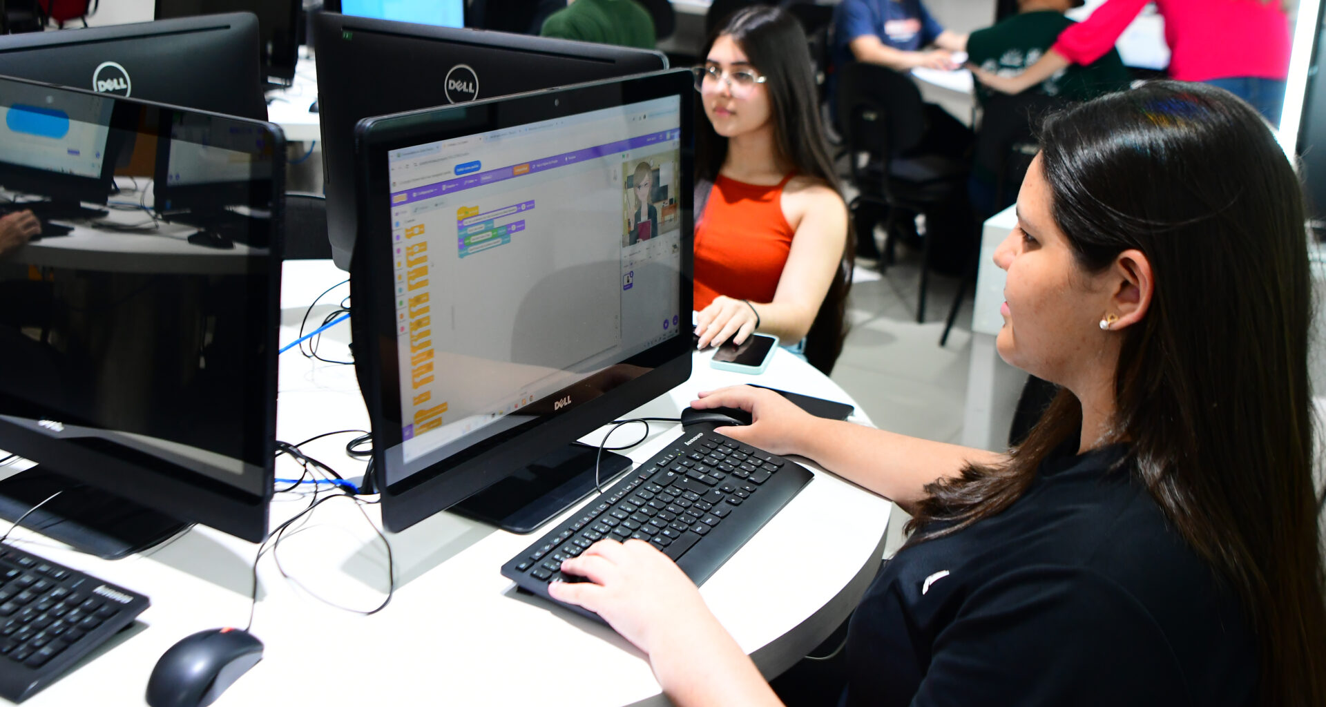 Duas estudantes da Unoeste utilizando computadores em laboratório de informática, desenvolvendo atividades de programação em ambiente acadêmico.