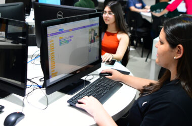 Duas estudantes da Unoeste utilizando computadores em laboratório de informática, desenvolvendo atividades de programação em ambiente acadêmico.