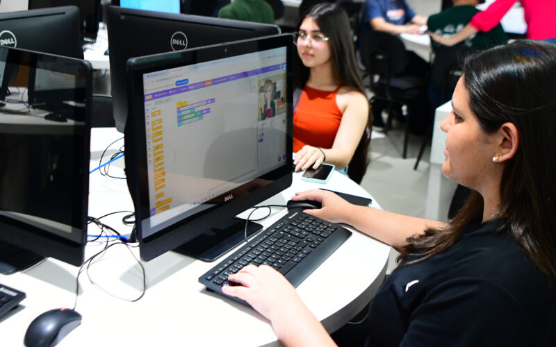 Duas estudantes da Unoeste utilizando computadores em laboratório de informática, desenvolvendo atividades de programação em ambiente acadêmico.