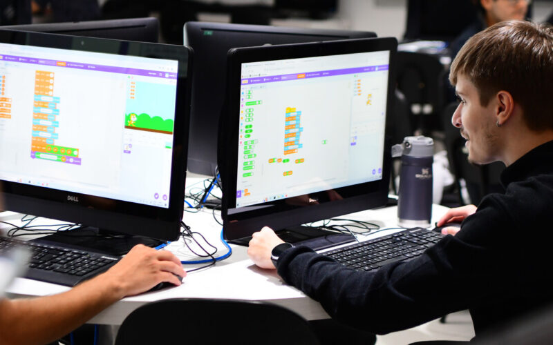 Estudantes de Sistemas de Informação da Unoeste em laboratório de informática, utilizando computadores para desenvolver e testar sistemas e aplicações digitais durante atividade prática.