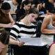 Estudantes concentrados realizando prova de vestibular em sala de aula, escrevendo e analisando questões nas folhas, demonstrando foco, gestão de tempo e preparação para o exame.
