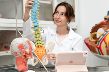 Estudante da área da saúde observa modelo anatômico da coluna vertebral e pelve em laboratório, ilustrando o ambiente de aprendizado do curso de Medicina.