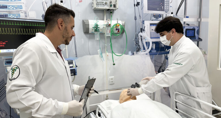 Fisioterapeutas em unidade de terapia intensiva realizam manejo de vias aéreas em paciente simulado, utilizando equipamentos hospitalares como ventilador mecânico e monitor multiparamétrico, ilustrando a prática profissional na UTI.