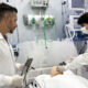 Fisioterapeutas em unidade de terapia intensiva realizam manejo de vias aéreas em paciente simulado, utilizando equipamentos hospitalares como ventilador mecânico e monitor multiparamétrico, ilustrando a prática profissional na UTI.