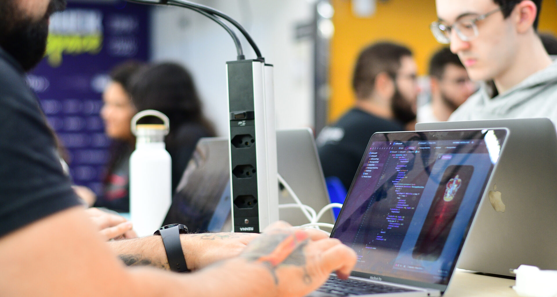 Estudantes da Unoeste trabalhando em notebooks com códigos de programação durante atividade prática em ambiente colaborativo, representando o uso de tecnologia e inteligência artificial no mercado de trabalho.