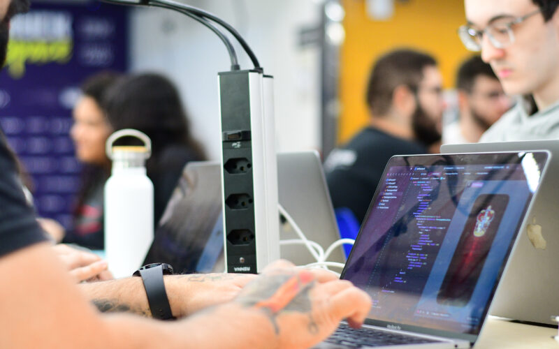 Estudantes da Unoeste trabalhando em notebooks com códigos de programação durante atividade prática em ambiente colaborativo, representando o uso de tecnologia e inteligência artificial no mercado de trabalho.