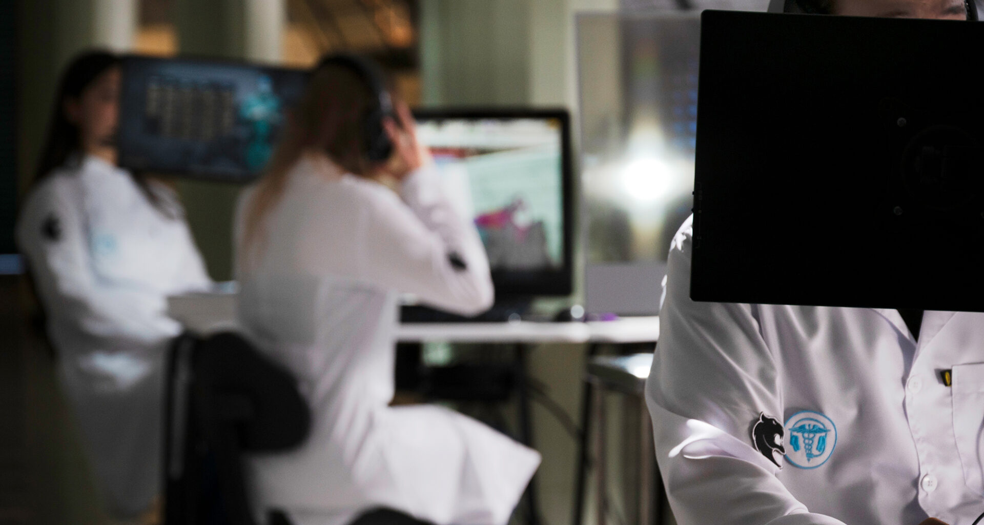 Estudantes de Medicina utilizando computadores e tecnologia digital em ambiente de simulação, demonstrando o uso de recursos tecnológicos e jogos aplicados ao aprendizado médico.