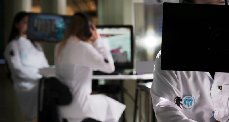 Estudantes de Medicina utilizando computadores e tecnologia digital em ambiente de simulação, demonstrando o uso de recursos tecnológicos e jogos aplicados ao aprendizado médico.