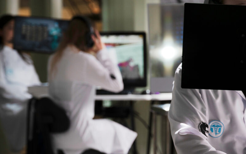 Estudantes de Medicina utilizando computadores e tecnologia digital em ambiente de simulação, demonstrando o uso de recursos tecnológicos e jogos aplicados ao aprendizado médico.