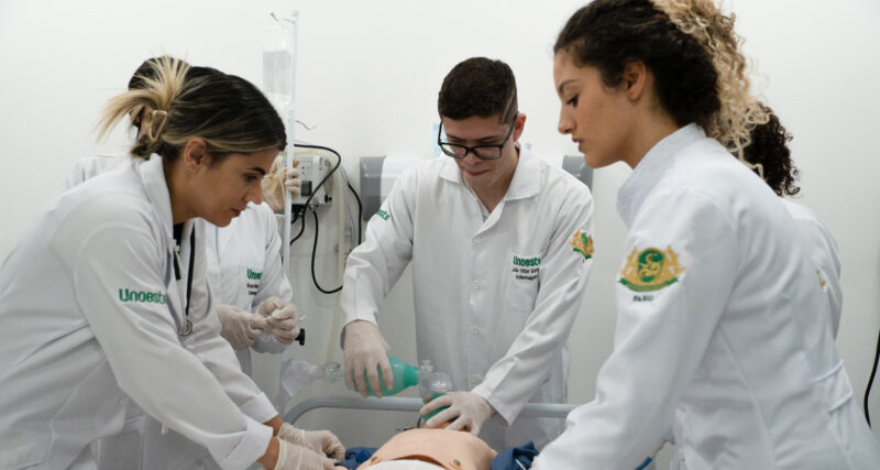 Estudantes de Enfermagem da Unoeste realizam treinamento prático em laboratório, utilizando manequim para simulação de atendimento com suporte respiratório, em ambiente hospitalar.
