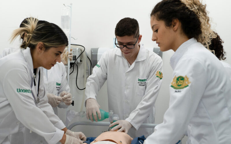 Estudantes de Enfermagem da Unoeste realizam treinamento prático em laboratório, utilizando manequim para simulação de atendimento com suporte respiratório, em ambiente hospitalar.