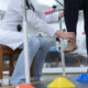 Pessoa em sessão de fisioterapia realizando exercício de equilíbrio e reabilitação dos membros inferiores, com acompanhamento de profissional de saúde em ambiente clínico equipado.