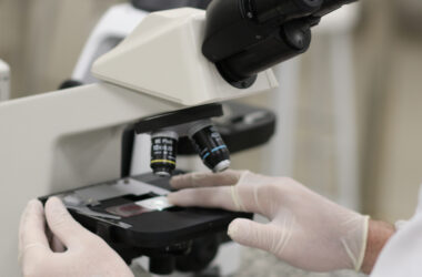 Pessoa utilizando microscópio em laboratório, com luvas, analisando lâmina com amostra para exame de citologia.