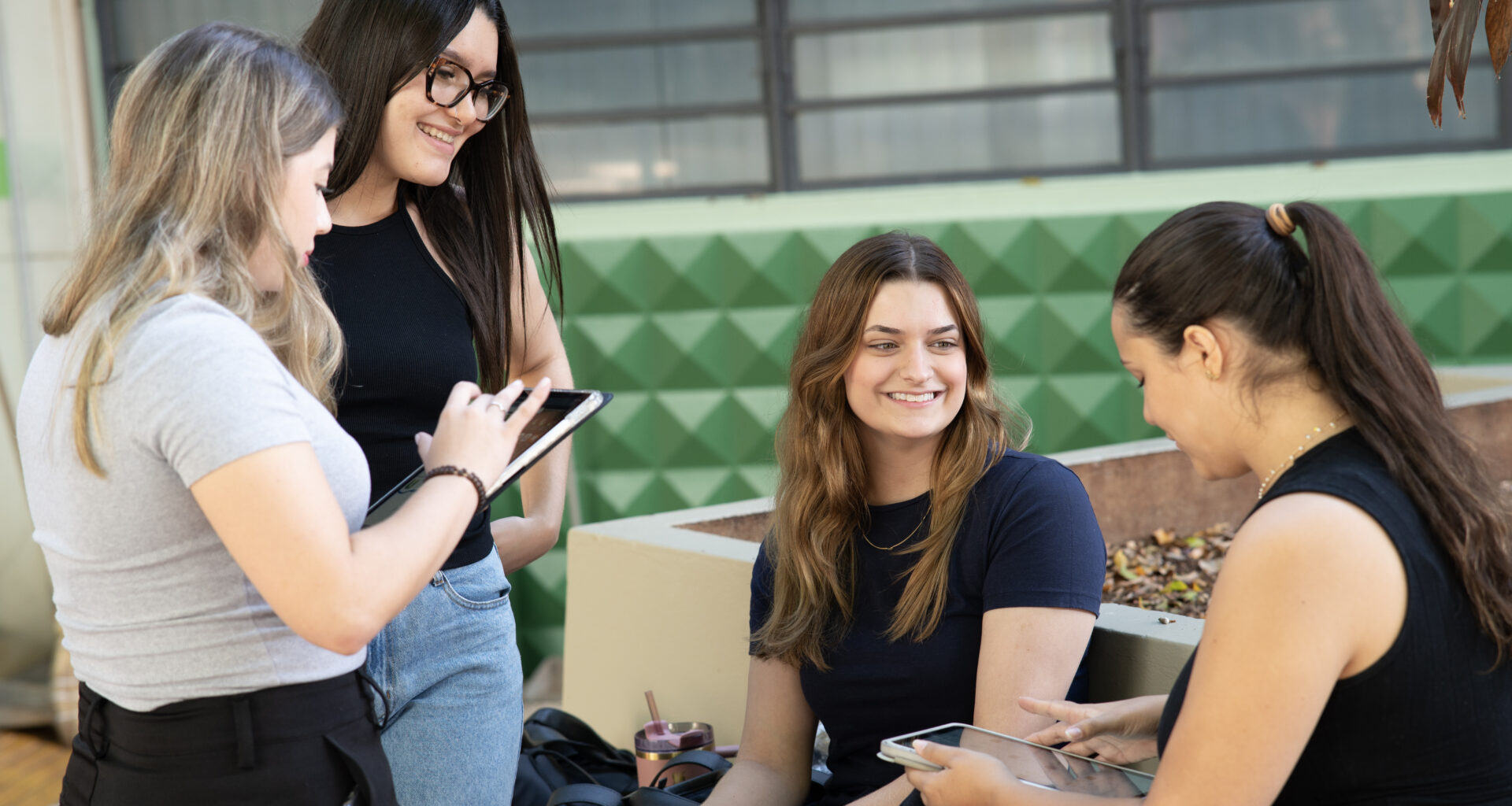 Grupo de estudantes conversando e estudando ao ar livre no campus universitário, utilizando tablets e materiais digitais durante a preparação para o Enem.