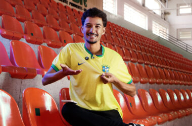 Homem sentado em arquibancada e usando camisa da seleção brasileira masculina de futebol.