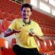 Homem sentado em arquibancada e usando camisa da seleção brasileira masculina de futebol.