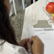 Estudante de Psicologia da Unoeste escreve anotações em um receituário durante atividade prática, ao lado de frutas utilizadas em dinâmica sobre alimentação e saúde.
