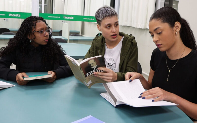Estudantes reunidas em sala de estudos da Unoeste, lendo livros e debatendo conteúdos relacionados à Psicologia e comportamento humano.