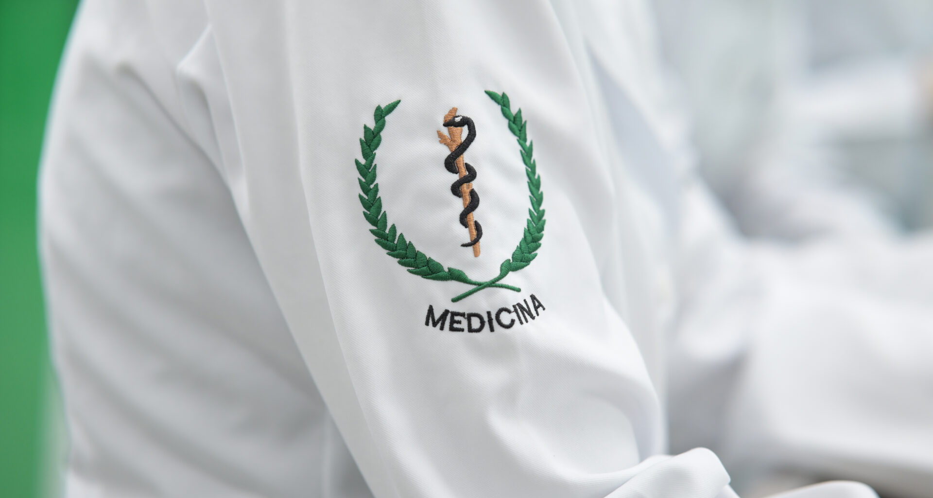 Detalhe do jaleco de estudante de Medicina com bordado do símbolo da profissão na manga, representando a formação médica e a preparação para atuar na área da saúde.
