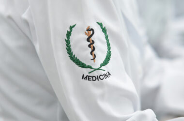 Detalhe do jaleco de estudante de Medicina com bordado do símbolo da profissão na manga, representando a formação médica e a preparação para atuar na área da saúde.