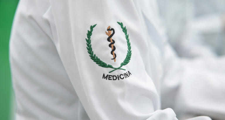 Detalhe do jaleco de estudante de Medicina com bordado do símbolo da profissão na manga, representando a formação médica e a preparação para atuar na área da saúde.