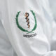 Detalhe do jaleco de estudante de Medicina com bordado do símbolo da profissão na manga, representando a formação médica e a preparação para atuar na área da saúde.